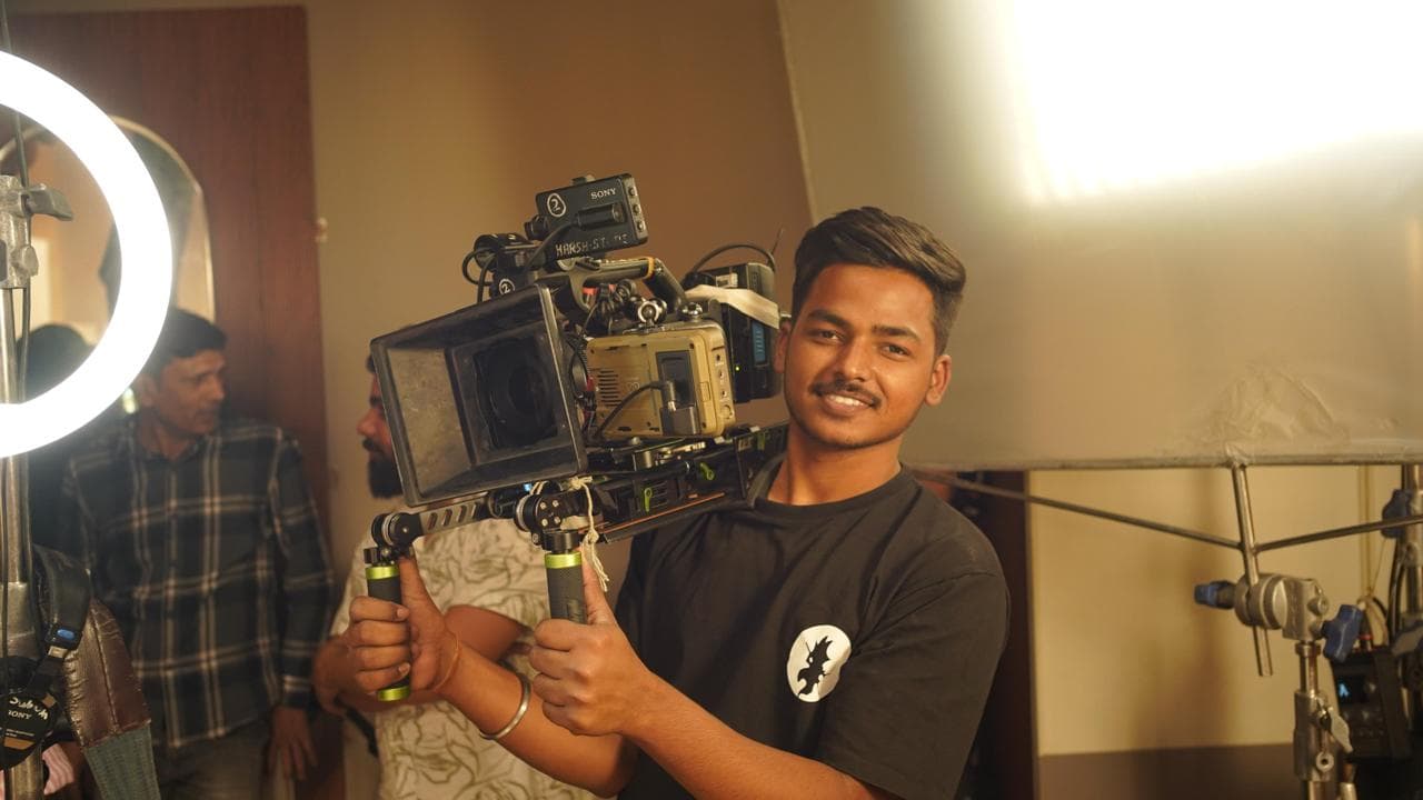 Crew member carrying a camera rig beside a ring light